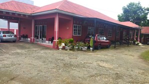 A red building with a covered porch, a car, and potted plants. - Hotel O Wisma Phinisi Syariah Near Mall of Pinrang Sejahtera (Pinrang)