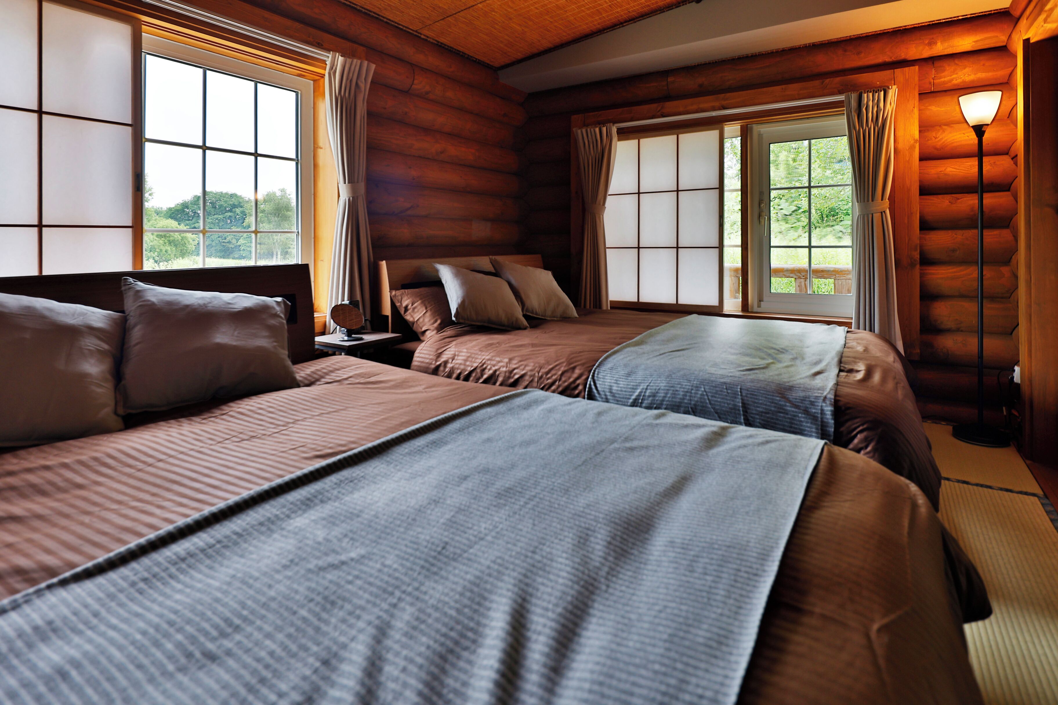 A log cabin bedroom with two beds, large windows, and a lamp.