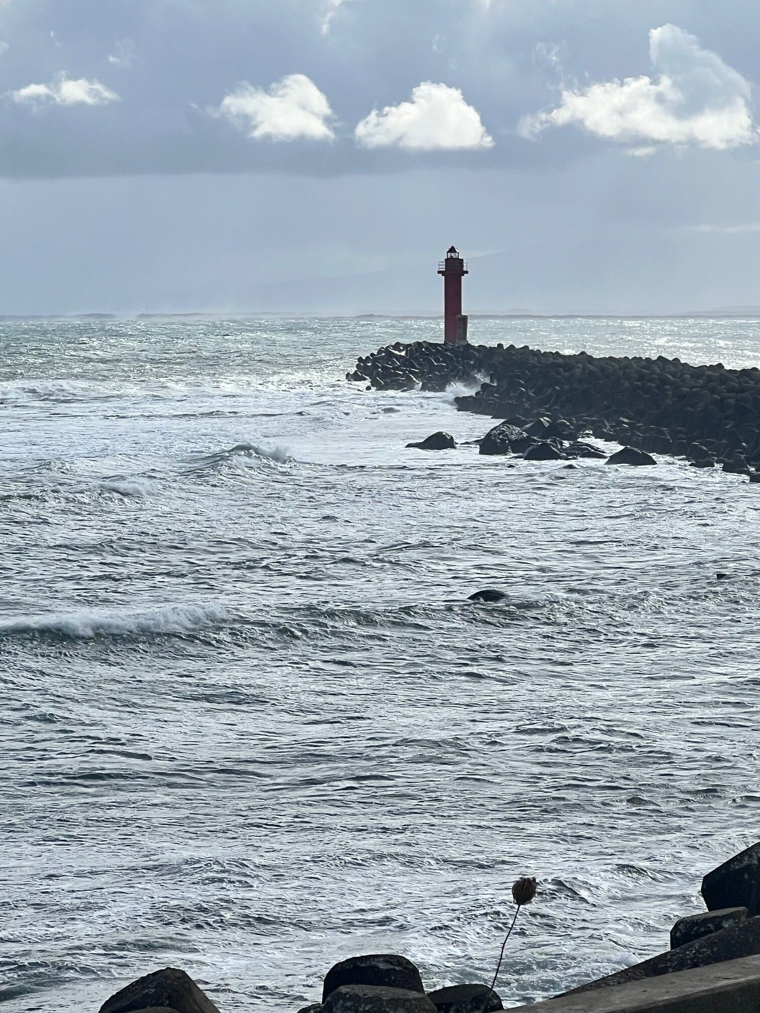 Um farol em um afloramento rochoso, com ondas batendo nele.