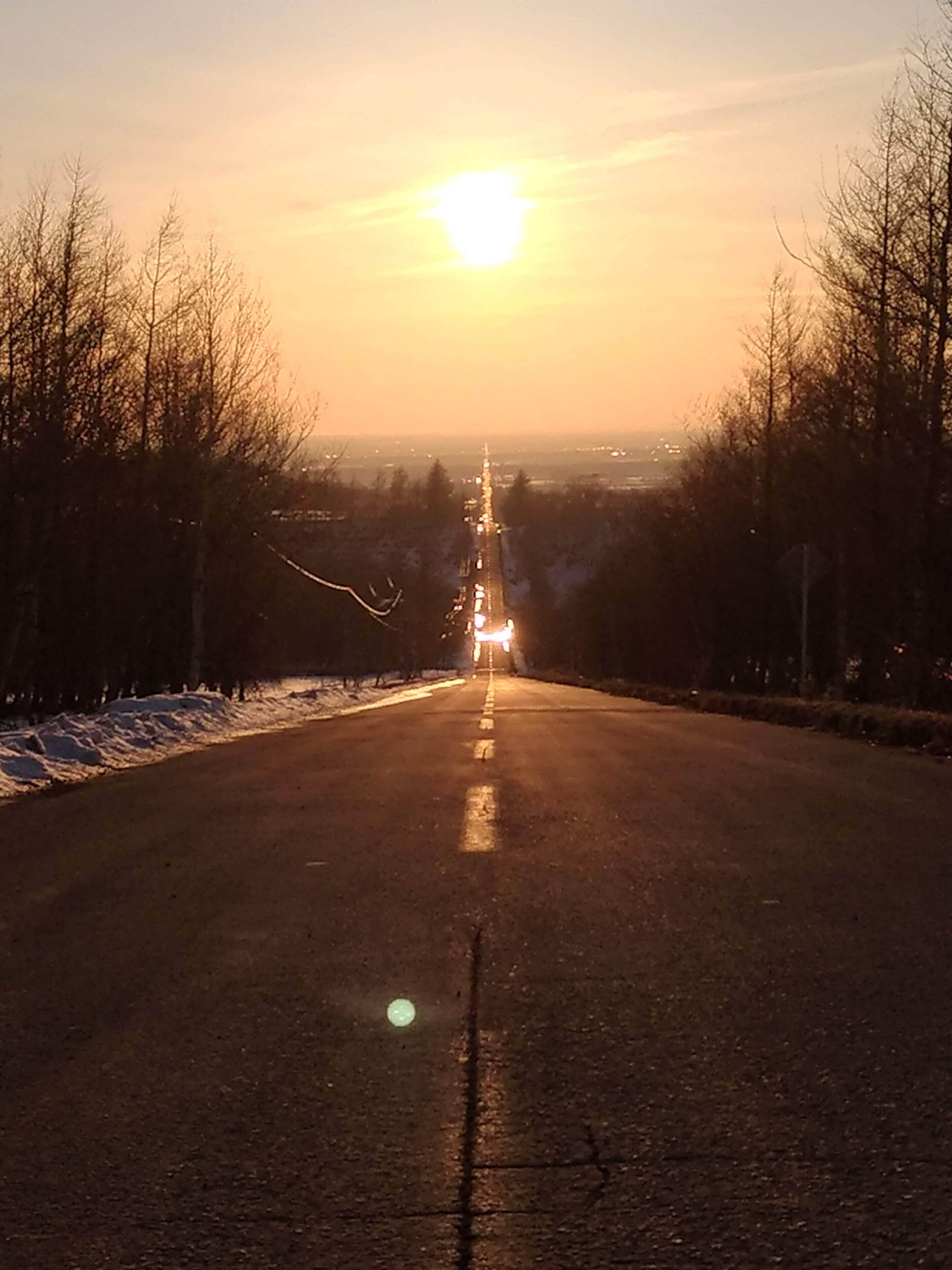 Een weg die naar een ondergaande zon leidt, met voertuigen in de verte.
