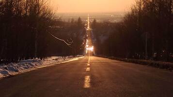 Een weg die naar een ondergaande zon leidt, met voertuigen in de verte.