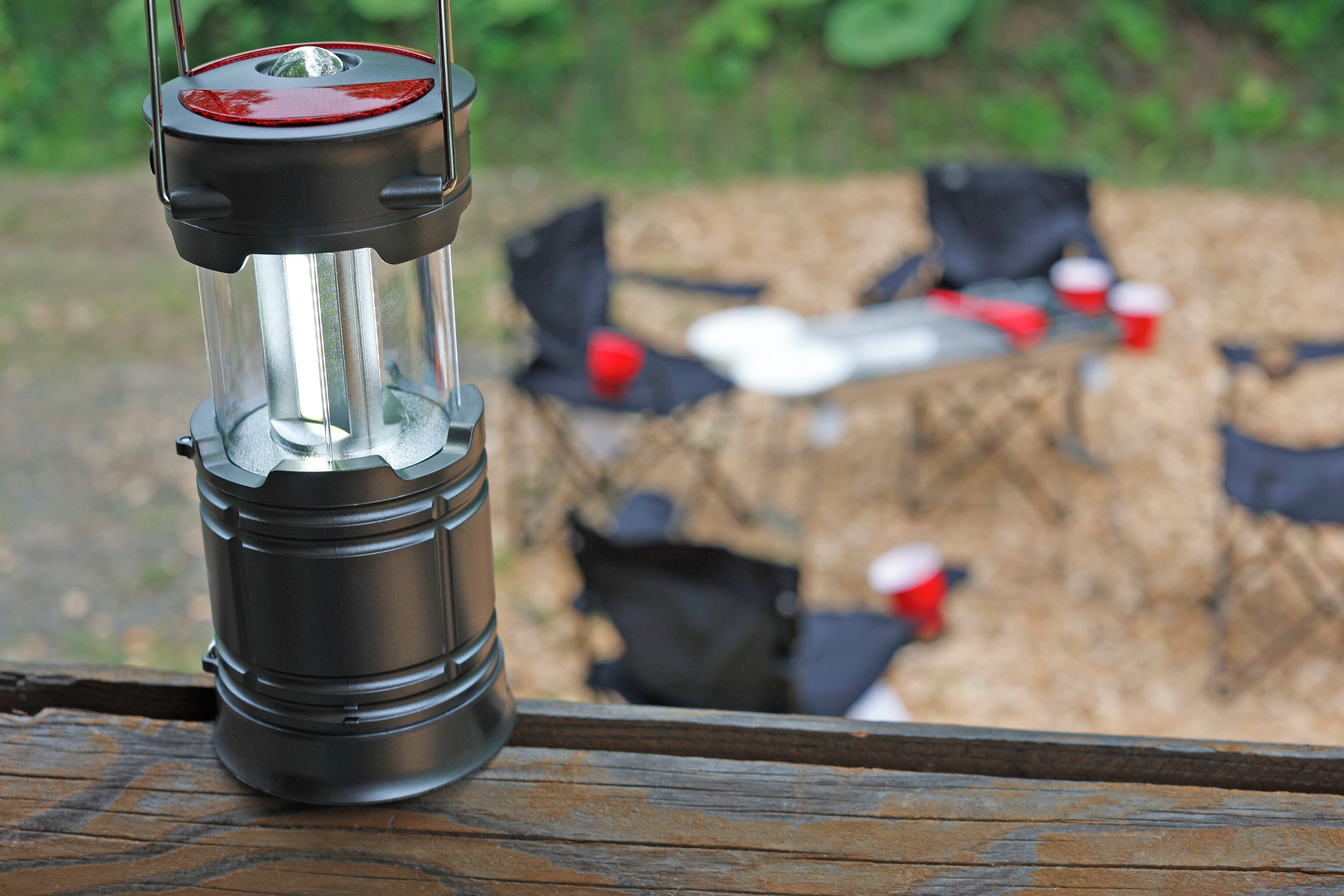 A lantern on a wooden surface with a blurred background of outdoor seating and tables.