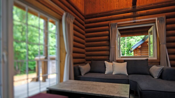 A log cabin interior with a sofa, a table, and a window overlooking greenery. - THE LODGE ABASHIRI (Abashiri)