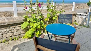 Une terrasse en bord de mer avec une table et des chaises, un mur en pierre et des plantes en fleurs.