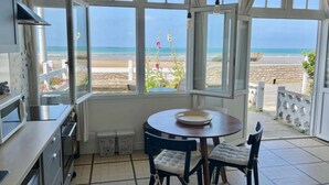 Une cuisine avec vue sur la plage, une table à manger avec des chaises et une grande fenêtre avec des rideaux.