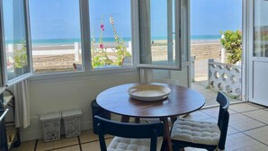 Un coin repas avec une table et des chaises, de grandes fenêtres donnant sur la plage et une plante en pot.