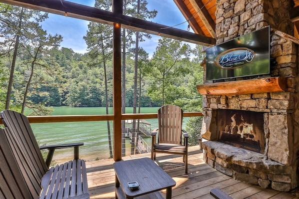 A cabin with a stone fireplace, wooden deck, and a view of a lake.