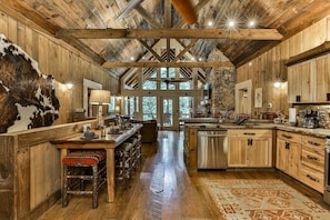 A rustic interior with wooden walls, a stone fireplace, a dining area, and a kitchen.
