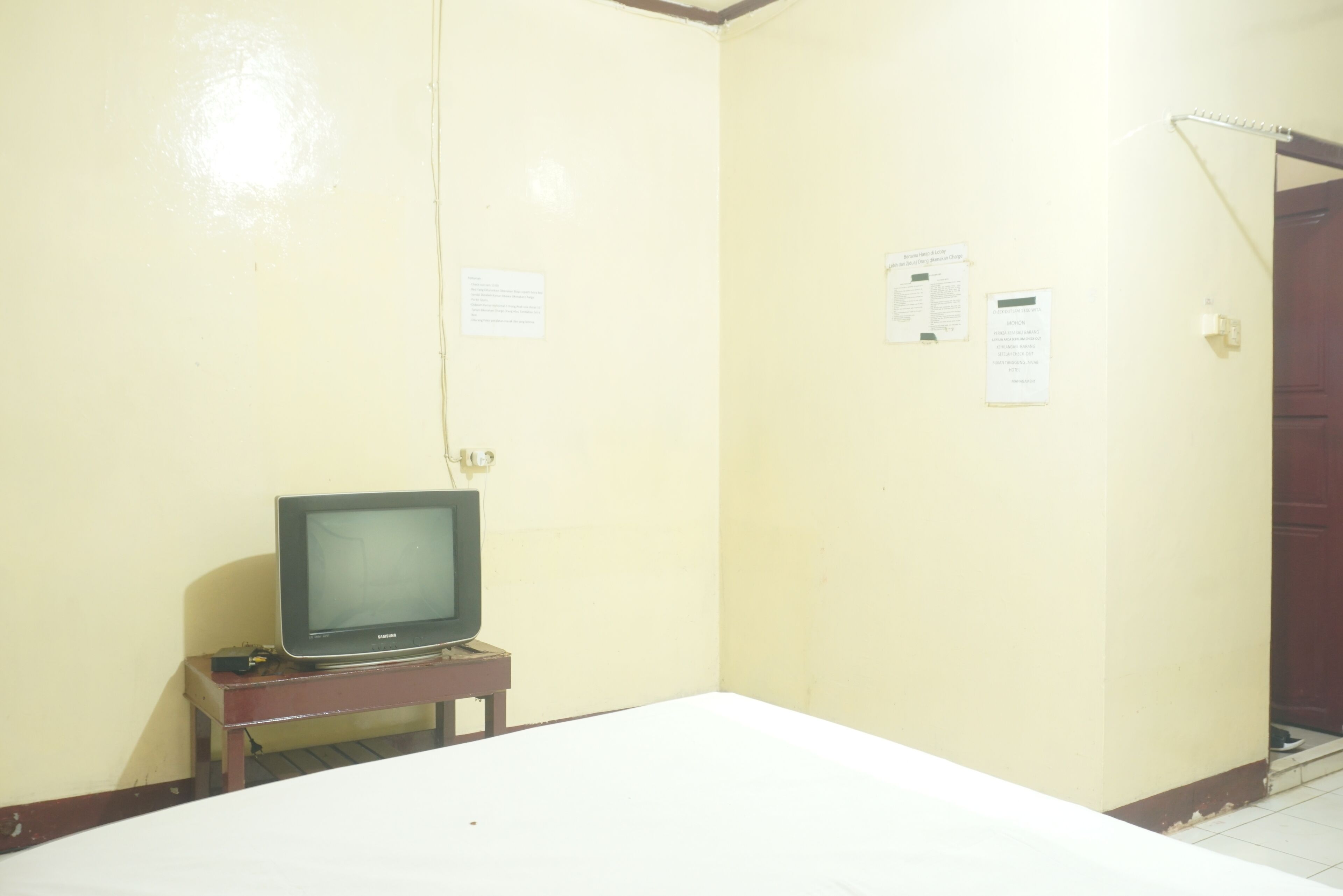A room with a bed, a television on a small table, and two notices on the wall.