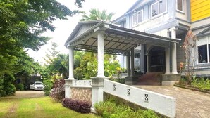 A covered porch with columns, a stone wall with the letters "SSSS" on it, and a pathway leading to a building with a yellow wall. - Hotel O Rumah Massagena Syariah Near Gedung Olahraga Enrekang (Makassar)