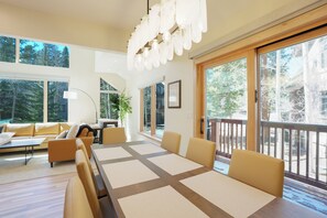 A spacious living area with a large dining table, comfortable seating, and large windows offering a view of the outdoors.