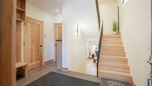 A hallway with a wooden staircase, a door with a small window, and a doormat with text.
