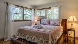 A bedroom with a bed, two bedside lamps, a bench, and a window with curtains. - Charming 2BR w/ Fire Pit + Mountain Views + Free Tickets (Hendersonville)
