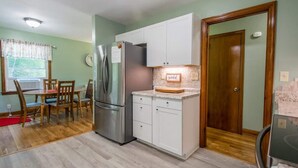 A compact kitchen with a refrigerator, white cabinets, a dining table with chairs, and a wooden door. - Charming 2BR w/ Fire Pit + Mountain Views + Free Tickets (Hendersonville)