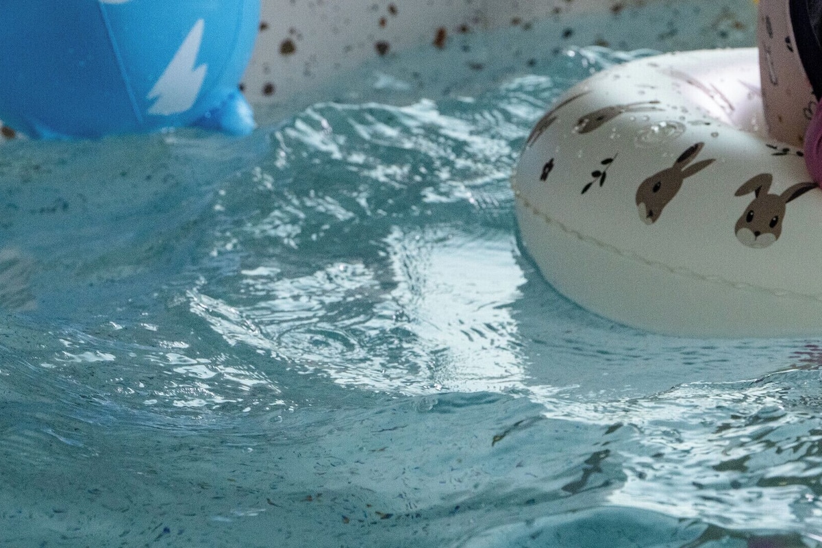 Eine Person im Wasser, ausgestattet mit einem weißen, aufblasbaren Ring mit Tierprints und rosafarbenen Schuhen.