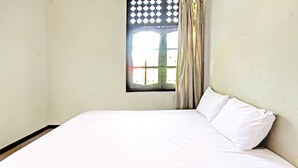 Une chambre avec un lit simple, une fenêtre à carreaux et un rideau.