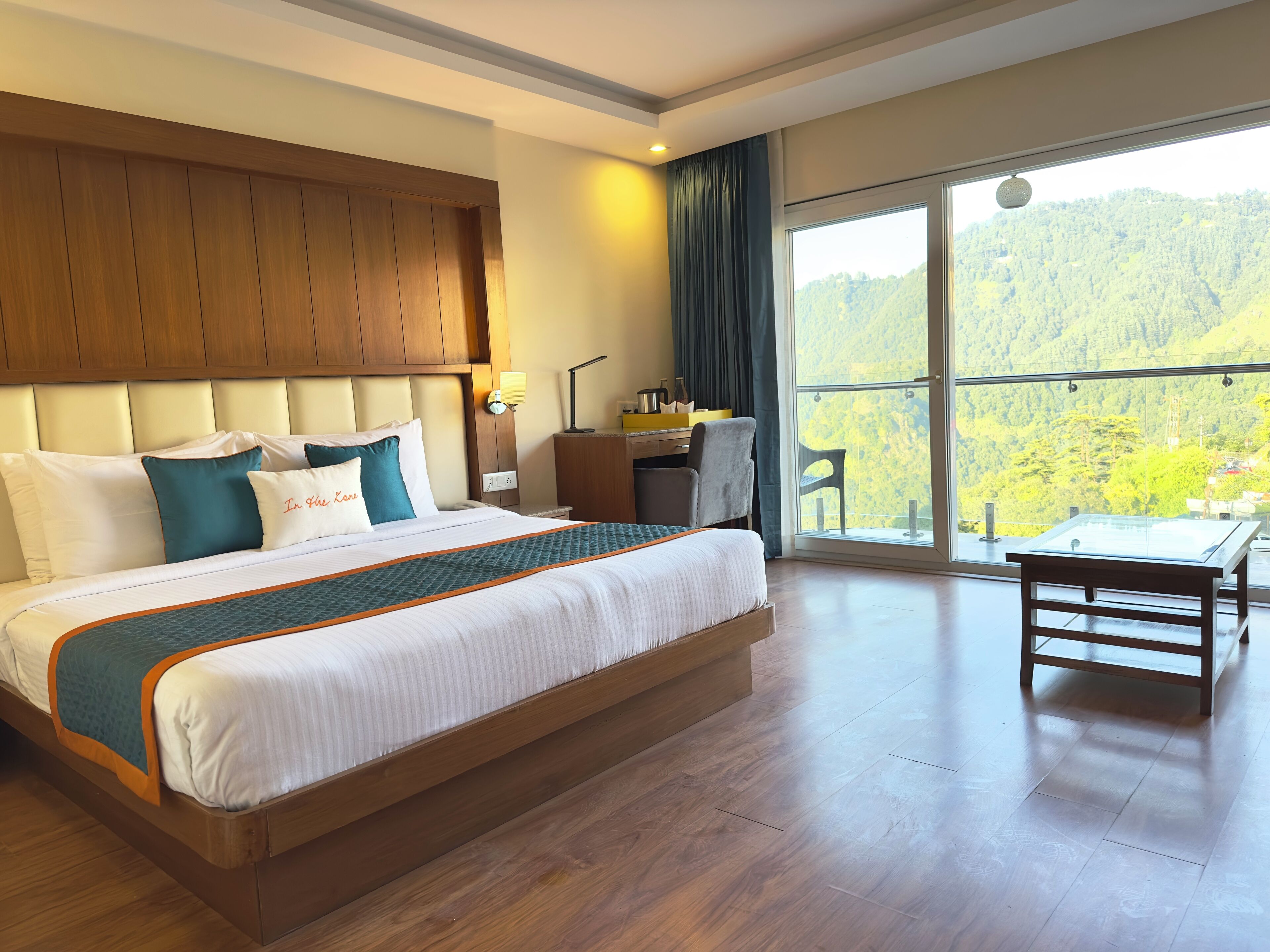 A hotel room with a large bed, a desk, and a view of a forested hillside.