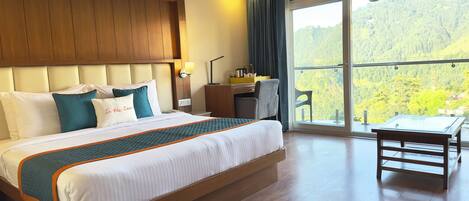 A hotel room with a large bed, a desk, and a view of a forested hillside.