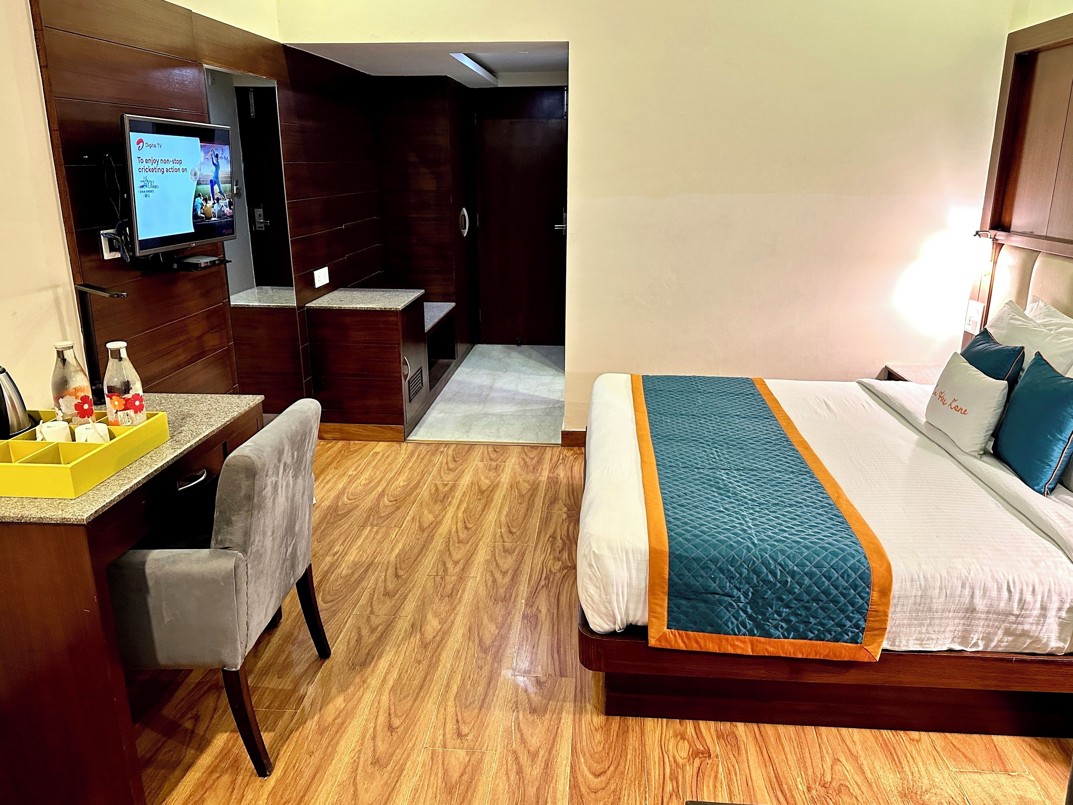 Une chambre d’hôtel avec un plancher en bois, un lit recouvert d’une couette bleue, un bureau avec une chaise, une télévision et un mini-bar.