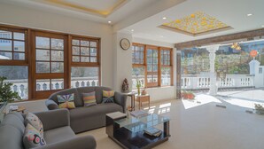 A spacious living room with a sofa, coffee table, and large windows offering a view of the outside. - Zone Connect by The Park Mussoorie (Dehradun)
