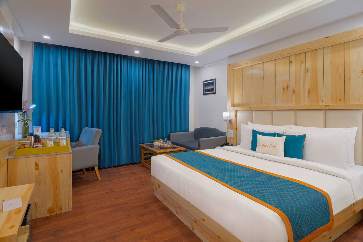 A hotel room with a bed, a desk, a chair, a TV, and a wooden headboard.