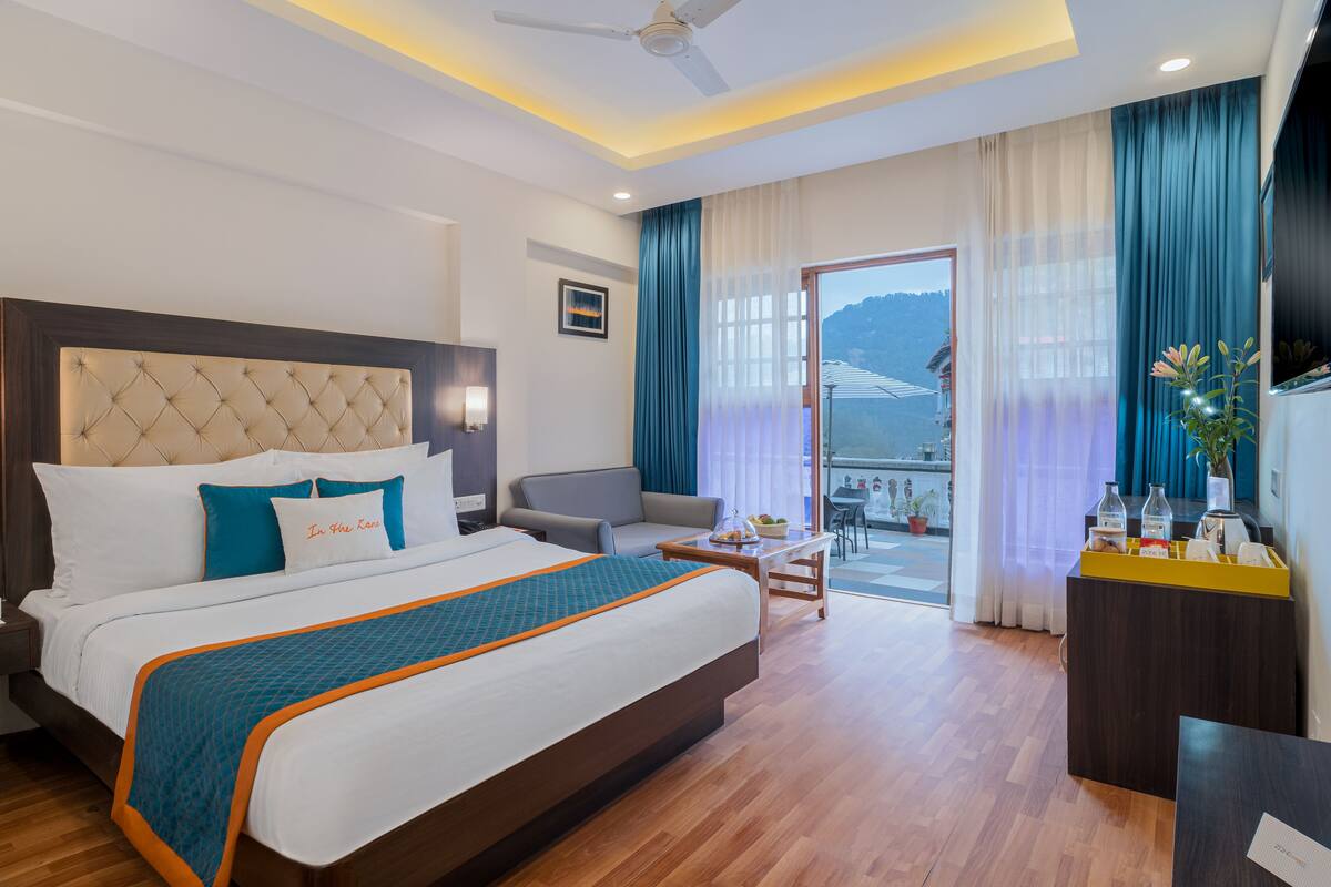 A hotel room with a large bed, a desk, a chair, and a balcony with a view.