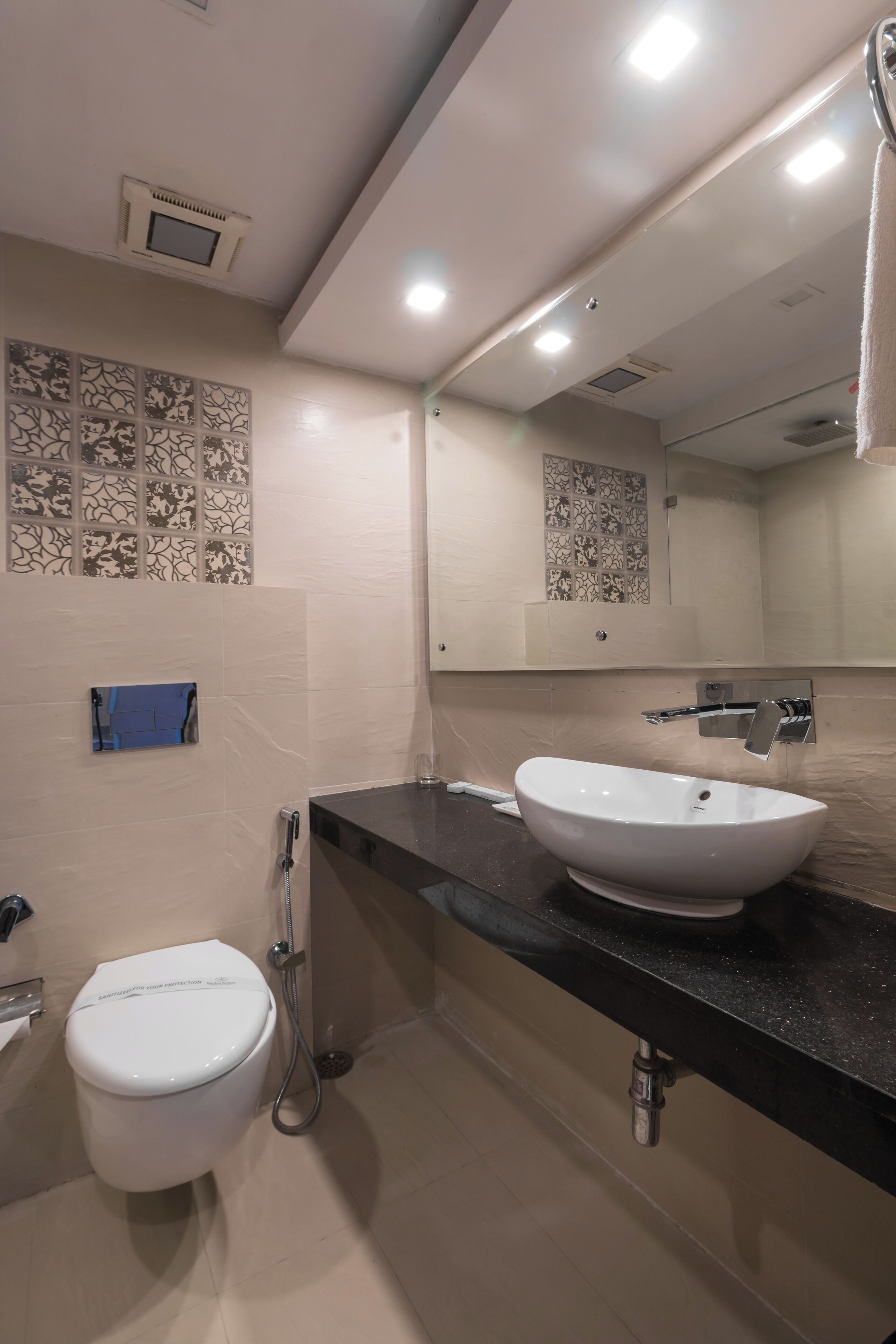 Une salle de bain moderne avec des toilettes blanches, un grand lavabo surmonté d’un miroir et des carreaux décoratifs sur les murs.
