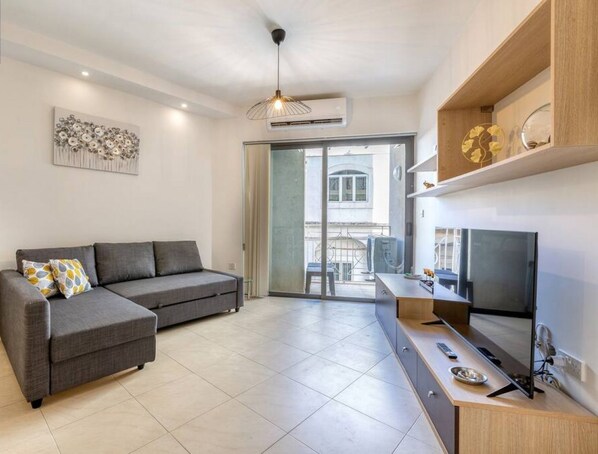 Una sala de estar moderna con un sofá gris, un televisor de pantalla plana y un comedor con una mesa de madera.