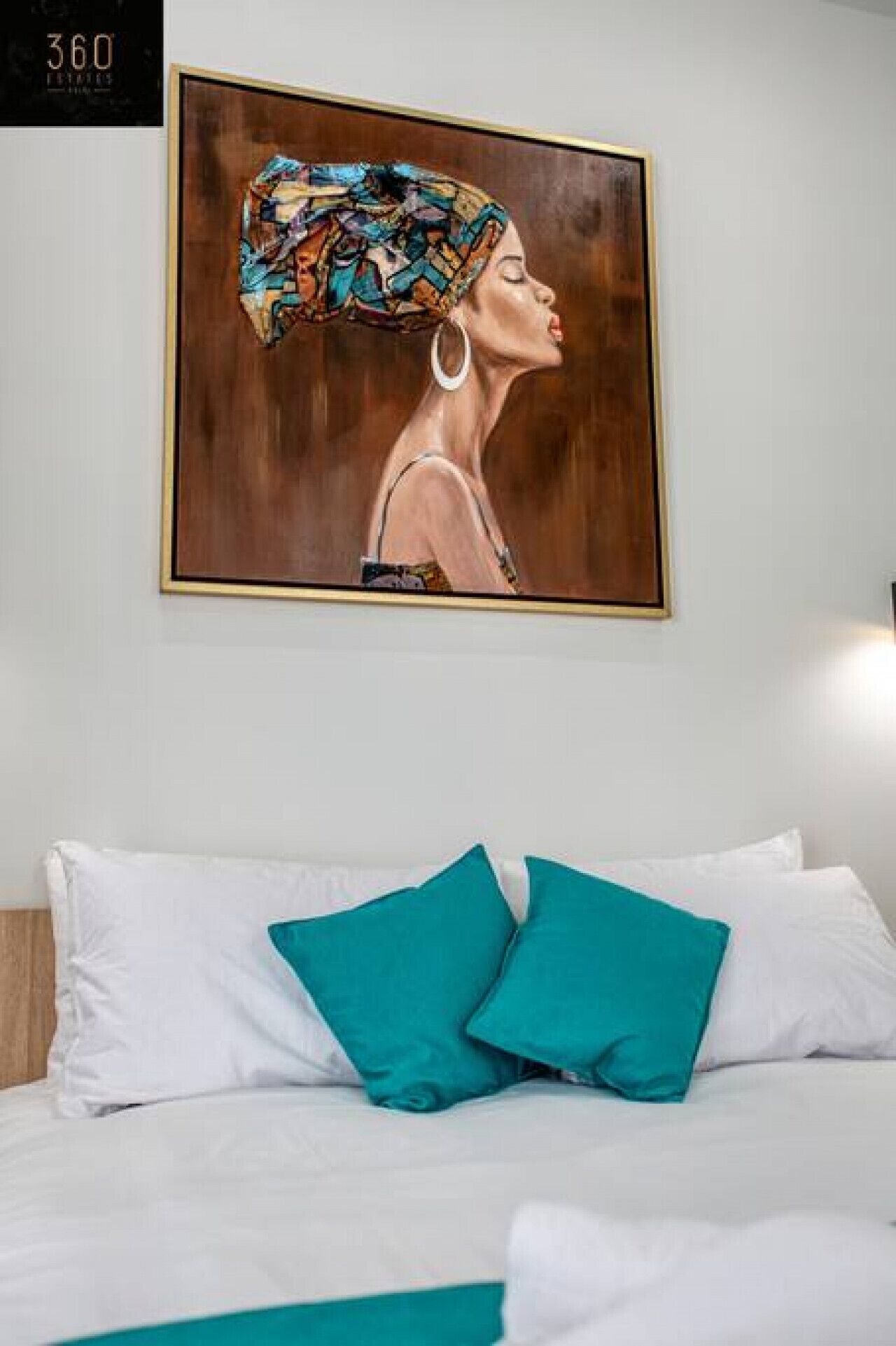 A hotel room with a bed, white bedding, and a teal pillow.