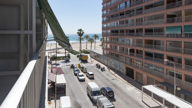 A multi-story hotel with balconies overlooking a busy street and beach.