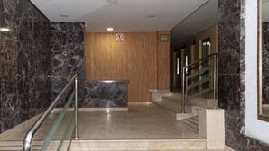 A modern lobby with marble walls, a wooden reception desk, and a staircase with metal railings.