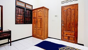 A room with a bed, wooden wardrobe, and a window with a metal grill. - OYO Life 92785 Wisma Trubus  Syariah (Tuban)
