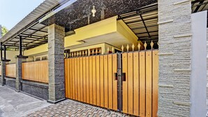 A gated entrance with a tiled walkway leading to a building with a stone facade and a yellow awning. - OYO Life 92785 Wisma Trubus  Syariah (Tuban)