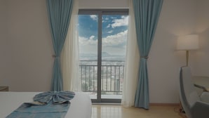 A hotel room with a bed, a chair, a lamp, and a view of a cityscape through a balcony. - Stay Easy Plus Hotel (Addis Ababa)