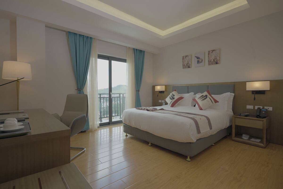 Ein Hotelzimmer mit einem großen Bett, einem Schreibtisch, einem Stuhl, einem Nachttisch und Blick ins Freie.