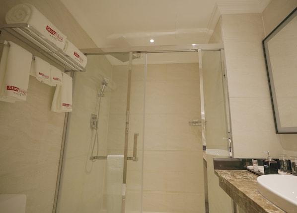 A hotel bathroom with a glass-enclosed shower, a sink with a marble countertop, and multiple towels hanging on a rack.