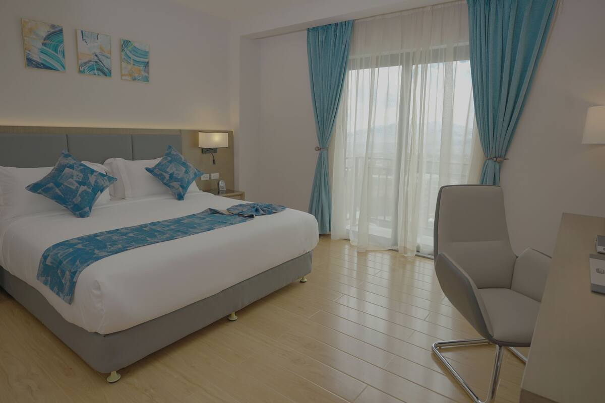 Ein Hotelzimmer mit Bett, Stuhl, Schreibtisch und einem Fenster mit Vorhängen.