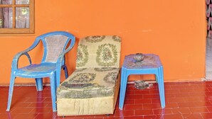 Una habitación con suelo de baldosas rojas, una silla de plástico azul, un sofá con estampado floral y un taburete pequeño azul.
