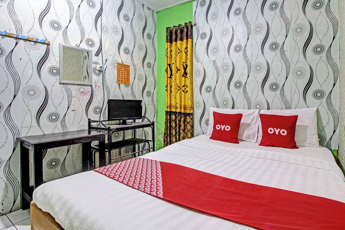 A hotel room with a bed, a desk, a chair, a TV, and patterned wallpaper.