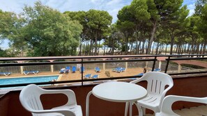 Ein Balkon mit Pool, Liegestühlen und Blick auf Strand und Bäume.