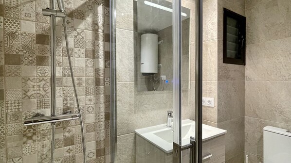 Ein modernes Badezimmer mit Duschabtrennung aus Glas, einem weißen Waschbecken und einer Toilette.