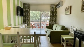 Een kamer met een eettafel, stoelen, een bank, een televisie en een balkon met plastic stoelen.