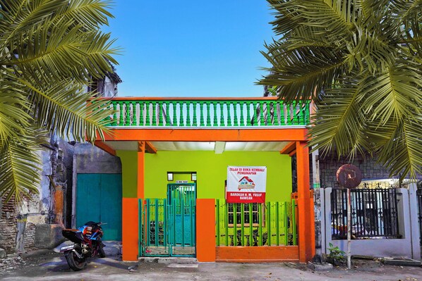 A building with a green and orange facade, a signboard, and a motorcycle parked in front.