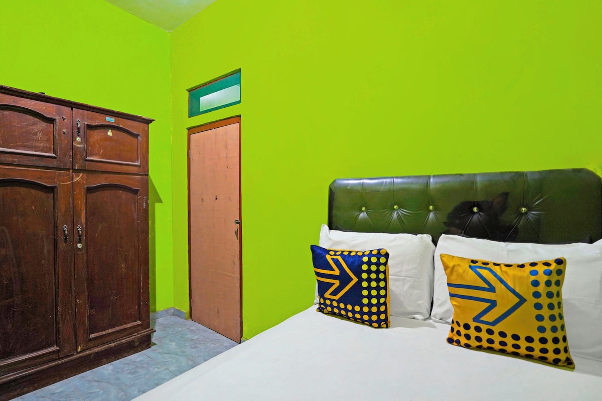 A room with a bed, two pillows with arrow designs, a wooden wardrobe, and a green wall.