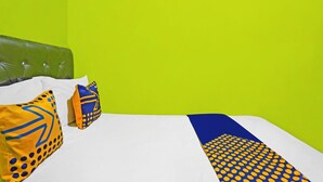 Una cama con ropa blanca, dos almohadas con diseños azules y amarillos, y un cabecero tapizado en verde.