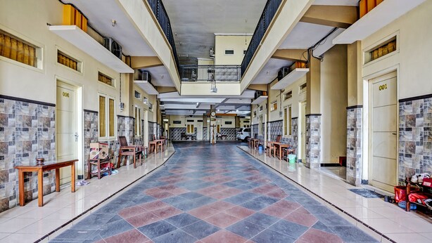 Ein Hotelgang mit Fliesenboden, mehreren Türen und einer zentralen Treppe.