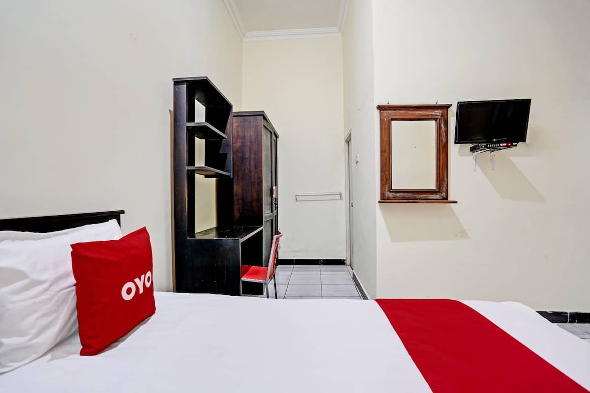 Une chambre d’hôtel avec un lit, un oreiller rouge, un téléviseur fixé au mur et une armoire en bois.