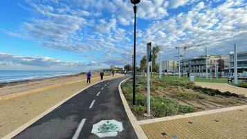 Un camí pavimentat amb un carril bici, una platja i edificis moderns al fons.