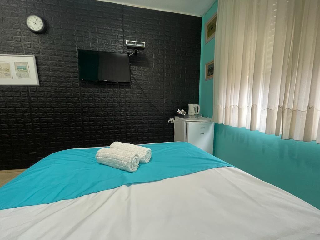 Une chambre d’hôtel équipée d’un lit, d’une horloge, d’une télévision et d’une petite kitchenette.