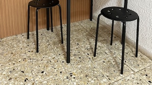 A small, dark wooden table with a kettle and a potted plant on top. There are two black stools in front of the table. - Breezot Yam (Nahariya)